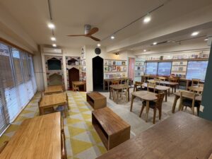 第13回マワリテメグルご縁日イベント会場の全体風景。木製のテーブルと椅子が並び、やさしい照明と窓の光に包まれた温もりある空間。